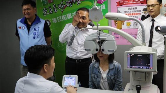 侯友宜陪長輩陳淑芳驗光 自己也蒙起一隻眼睛 一旁的林國春議員也不自覺地瞇起來